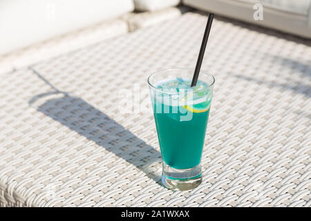 Blue Curacao Strand Cocktail mit frischer Zitrone, stehend auf einem Bootssteg, mit Palmen im Hintergrund Stockfoto