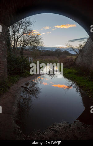 Britische Landschaft auf einer winterlichen Nachmittag unter dem Gleis Bogenbrücke gesehen; blauer Himmel wunderschön in einer großen Pfütze auf dem Boden nieder. Stockfoto