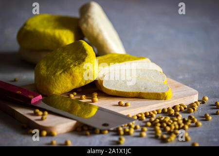 Frischer Tofu ist auf einem hölzernen Schneidebrett und Sojabohnen Samen auf dem Tisch verstreut in Scheiben geschnitten. Gesunde Ernährung Konzept. Stockfoto