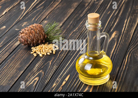 Zeder Öl in Glasflasche mit Haufen von Muttern und Pine Cone auf hölzernen Tisch Stockfoto