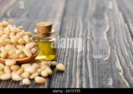 Wesentliche zeder Öl in kleinen Glasflasche mit Haufen der Muttern auf hölzernen Tisch Stockfoto
