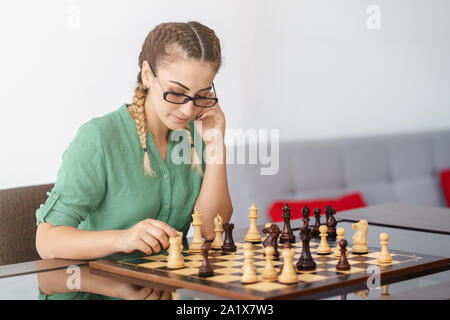Junge Frau mit Brille spielt Schach auf weißem Hintergrund. Stockfoto