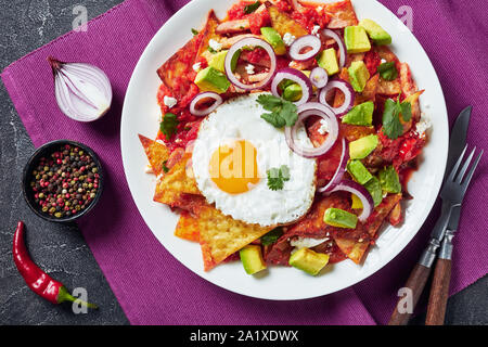 Nachos mit einem gebratenen sunny side up Ei, Schinken, zerbröckelt panela Käse, Avocado und Tomaten auf einer Platte auf einer konkreten Tabelle, mexikanische Gerichte, die Aussicht von ein Stockfoto