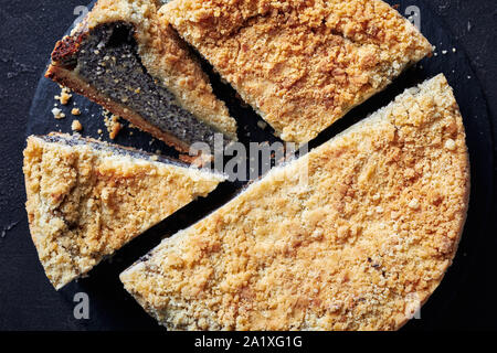 Mohn Streusel Käsekuchen in Scheiben geschnitten auf schwarzem Schiefer rundes Tablett auf einer konkreten Tabelle, Ansicht von oben, flatlay, close-up Stockfoto