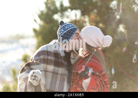 Ein liebevolles Paar in warmen Plaids Küsse holding Wunderkerzen in der Hand. Der Winterurlaub in einem verschneiten Wald. Stockfoto