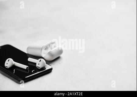 White wireless Bluetooth Ohrhörer oder Kopfhörer auf dem Smartphone mit Kunststoffgehäuse oder Box zur Aufbewahrung und zum Aufladen auf konkreten Hintergrund. Close Up. Cop Stockfoto