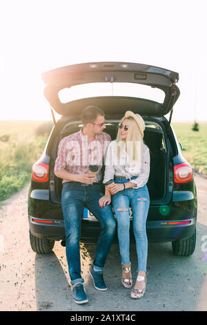 Junge Frau sitzt im Kofferraum mit ihrem Freund in Kaffee. Paar auf Straße Reise im Winter. Stockfoto