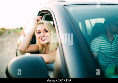 Portrait von Frau gehen auf einen Road Trip lehnte sich aus dem Fenster. Weibliche genießen Reisen in einem Auto mit ihrem Freund. Stockfoto