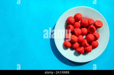 Rote Erdbeere zuckerhaltige Bonbons in weiße Platte auf Türkisfarbenem Hintergrund mit Kopie Raum Stockfoto