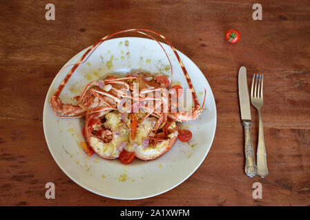 Salat von einem gekochten Languste garniert mit Olivenöl auf eine Platte stehend auf einem braunen Holztisch in Sizilien und Besteck Stockfoto