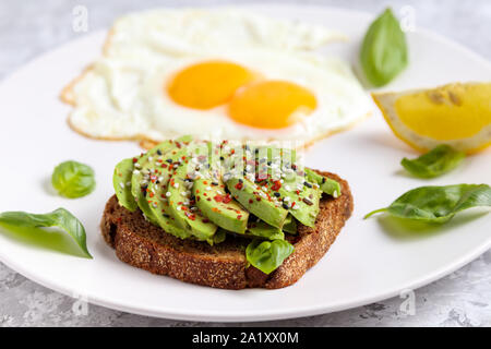 Avocado Frühstück. Ei sandwich Toast gesund essen. Frische vegetarische Snack auf weiße Platte. Roggenbrot mit Basilikum, Chili, Sesam und Zitrone. Vegane Kost Stockfoto