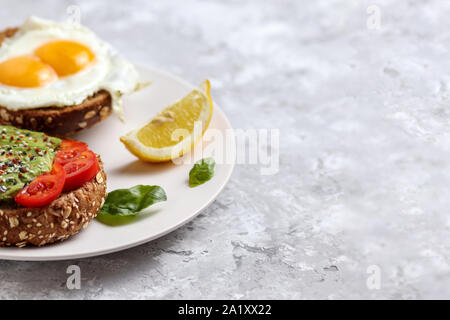 Avocado Mahlzeit. Gesund ei Toast auf Roggen Brot mit Tomaten. Vegetarischer Brunch Gericht. Herrlich grünen burger Rezept für Frühstück. Snack mit Tomaten und Stockfoto