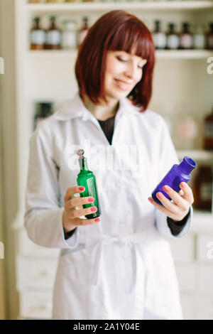 Attraktive junge Dame Apotheker mit einem reizenden Lächeln ständige Arbeitsgruppe und halten Glas vintage Flaschen von Arzneimitteln in der Apotheke Stockfoto