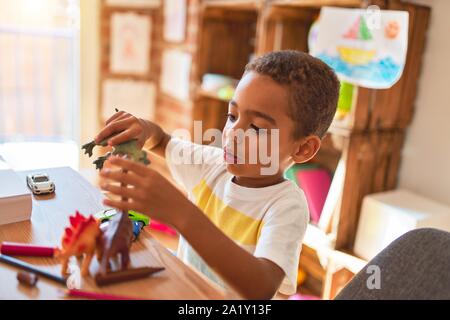 Schöne afrikanische amerikanische Kleinkind spielen mit Dinosaurier Spielzeug auf dem Schreibtisch im Kindergarten Stockfoto