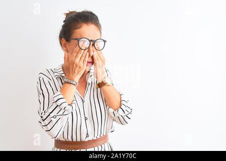 Mittleres Alter Geschäftsfrau tragen gestreiftes Kleid und Gläser über isoliert weißer Hintergrund reiben Augen für Ermüdung und Kopfschmerzen, schläfrig und müde Ausdr Stockfoto