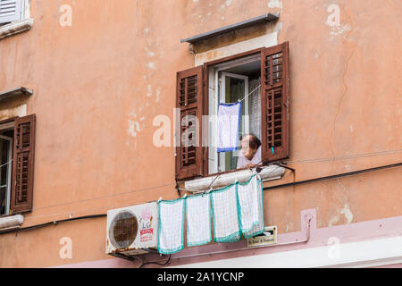 Eine ältere Frau gesehen Peering aus Ihrem Haus nach Wäscherei auf ihre Linie in Rovinj, Kroatien im September 2019. Stockfoto