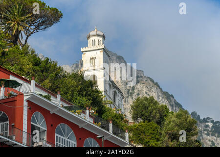 Insel CAPRI, ITALIEN - AUGUST 2019: Kirchturm gegen eines der hohen Berge auf der Insel Capri. Stockfoto