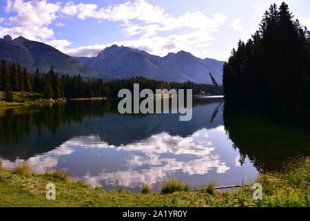 Eine glatte Oberfläche auf dem Johnson Lake spiegelt die Schönheit der felsigen Berge in der Nähe von Banff, Alberta, Kanada, wider. Stockfoto