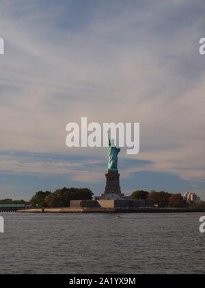 Beleuchtete Freiheitsstatue im Hafen von New York im September 2109. Ferner cargo Kräne am Hafen von Bayonne, NJ. Stockfoto