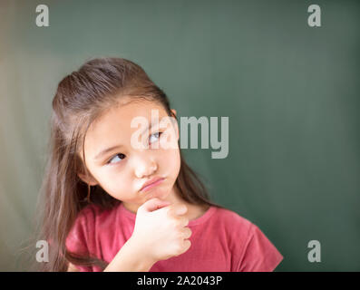 Kleines Mädchen stehend gegen Schiefertafel Hintergrund Stockfoto