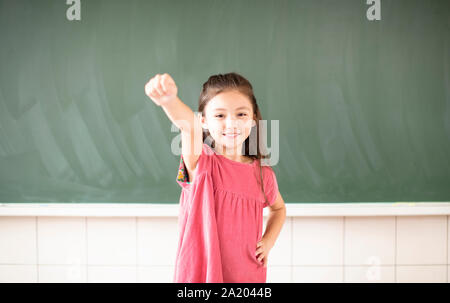 Gerne kleine Mädchen stehend gegen Schiefertafel Hintergrund Stockfoto