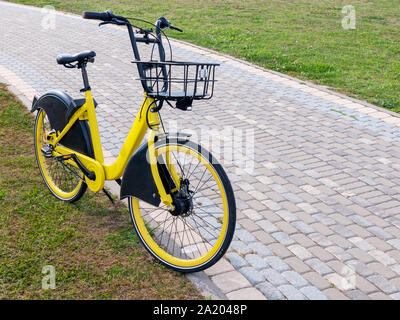 Yellow Bike mit Essen Korb stehend auf grünem Gras in der Nähe von Fußweg. Stadt Fahrräder zu mieten Stockfoto