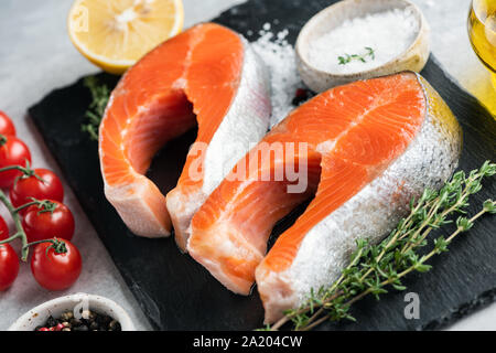 Zwei Lachssteaks, Gewürze und Kräuter zum Kochen auf schwarzem Schiefer. Gesunde Ernährung Konzept. Selektiver Fokus Stockfoto