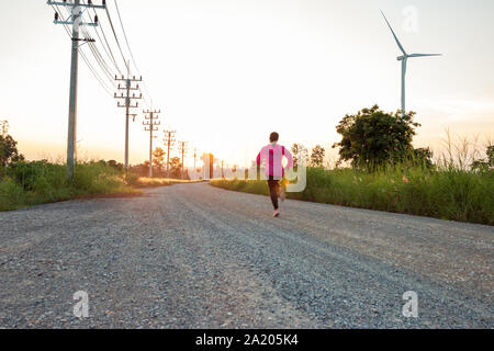 Den Sonnenuntergang am Abend, der Bereich der Windenergieanlage erzeugt saubere Energie Strom, eine Frau ist Joggen auf der Straße. Stockfoto