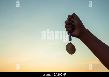 Konzepte der Sieg, Erfolg, Hände mit einem preisgekrönten Medaille auf schönen Sonnenuntergang Himmel Hintergrund. Stockfoto