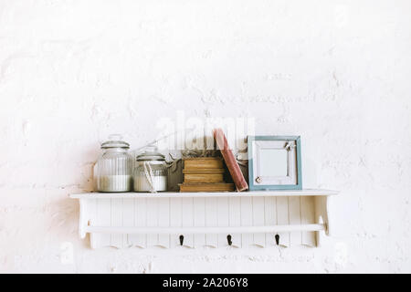 Handgefertigt aus Holz Regal mit Büchern, Bilderrahmen und Kerzen in Glasflaschen. Gemütliche rustikale Stil, weißen Hintergrund. Stuckverzierungen an der Wand. Stockfoto