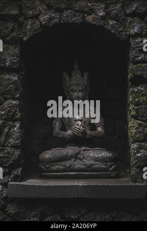 Balinesische Gottheit statuette auf dunklem Stein Hintergrund. Hinduistische Kultur in Bali. Handgefertigte Stein schnitzen. Stockfoto