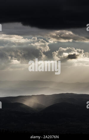 Sonnenstrahl scheint durch Wolken und Regen über die Berge in der Mitte der Schatten Stockfoto