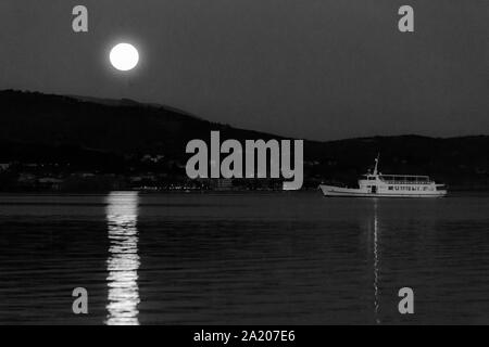 Vollmond über einige Hügel am Trasimeno See, perfekt auf dem Wasser mit einer Fähre, die in der Nähe Stockfoto