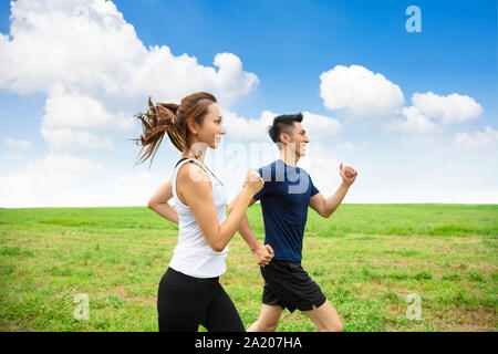 Glückliches junges Paar joggen und auf dem Gras laufen lassen Stockfoto