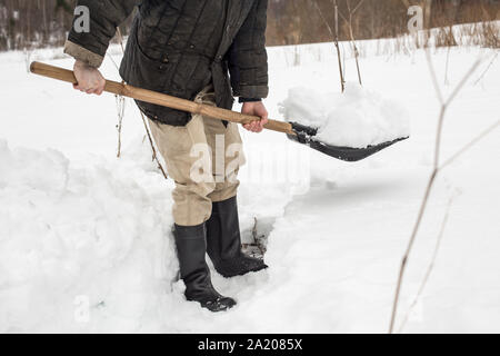 Mann schneeschaufeln von der Schiene, mit einem Spaten im Winter im Dorf Stockfoto