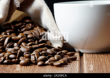Kaffee Bohnen in Säcke und leeren weißen Schale auf einem Holztisch Stockfoto