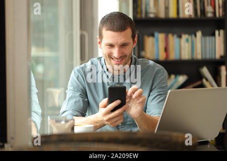 Vorderansicht Portrait Of Happy mit Smartphone und Laptop in ein Café oder nach Hause sitzen Mann Stockfoto