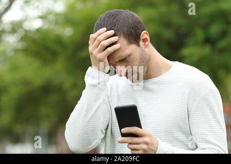 Traurig erwachsenen Mann Kontrolle smart phone Nachricht allein in einem Park Beschweren Stockfoto