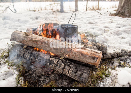 Kochen in einer Winterwanderung im Kessel über dem Feuer in der Verschneiten Kiefernwald beim Camping, aus dem Kessel, Dampf Stockfoto
