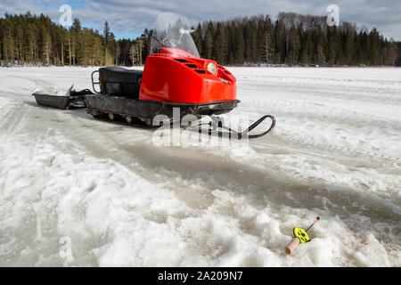 Im Winter Angelrute liegt auf dem Eis in der Nähe der Bohrung, und daneben ein Schneemobil Stockfoto