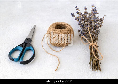 Natürliche hanf Kordel Kugel, Schere und trockenen Lavendel Blumenstrauß auf einer rauen Oberfläche in Weiß. Jute Schnur oder Flachs Garn. Grob rustikale Gewinde für Souvenirs. Stockfoto