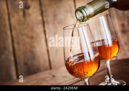Rich golden Sherry aus Andalusien Spanien geschüttet wurde in eine stilvolle wineglass in Nahaufnahme auf dem Hals der Flasche über Holz mit Kopie Raum Stockfoto
