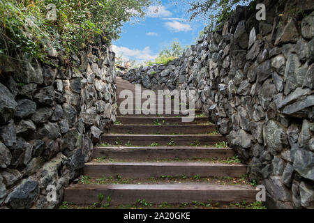 Eine lange, hohe Treppe mit Holzstufen Verlängerung nach oben in den blauen Himmel von Steinmauern umgeben. Business und Karriere Wachstum, die pa Stockfoto
