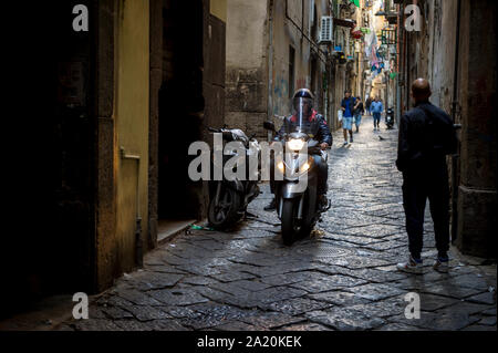 Neapel, Italien - OKTOBER, 2017: Motorroller und Fußgänger teilen sich eine schmale Fußgängerzone Gasse in der mittelalterlichen Centro Storico historische Zentrum. Stockfoto