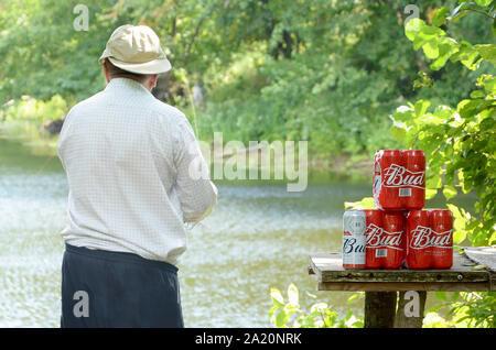 Kharkov, Ukraine - August 10, 2019: Budweiser Bud Bierdosen pack auf alten Tisch und Fischer am Fluss für den Hintergrund. Budweiser ist einer der beliebtesten Stockfoto