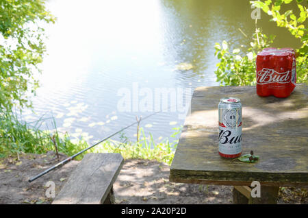 Kharkov, Ukraine - August 10, 2019: Budweiser Bud Bier kann auf alten hölzernen Tisch draußen am Fluss und grüne Bäume Hintergrund. Budweiser ist einer der Stockfoto