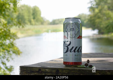 Kharkov, Ukraine - August 10, 2019: Budweiser Bud Bier kann auf alten hölzernen Tisch draußen am Fluss und grüne Bäume Hintergrund. Budweiser ist einer der Stockfoto