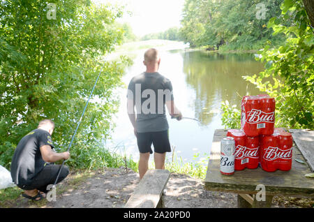 Kharkov, Ukraine - August 10, 2019: Budweiser Bud Bierdosen pack auf alten Tisch und Fischer am Fluss für den Hintergrund. Budweiser ist einer der beliebtesten Stockfoto