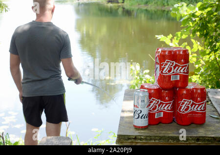 Kharkov, Ukraine - August 10, 2019: Budweiser Bud Bierdosen pack auf alten Tisch und Fischer am Fluss für den Hintergrund. Budweiser ist einer der beliebtesten Stockfoto