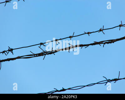 Nahaufnahme eines alten Handwerks rostigen Stacheldraht in mehreren Threads auf einem klaren, blauen Himmel gestreckt Stockfoto